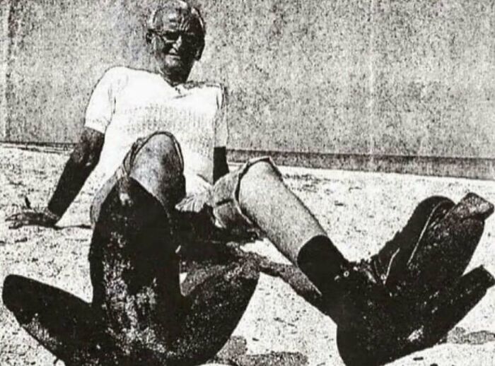 Man wearing large diving flippers, sitting on sand, a glimpse into interesting history facts.