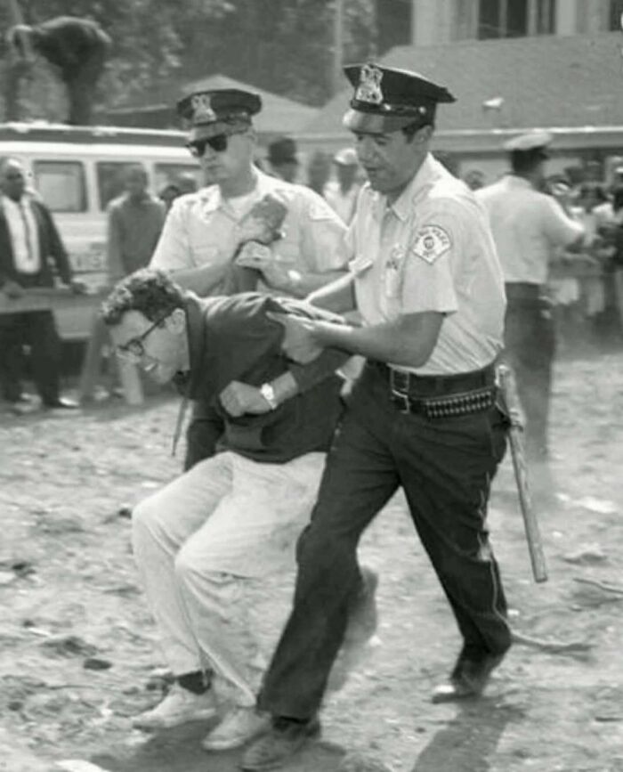 A man being arrested by two police officers in a historical event setting, capturing an interesting history moment.