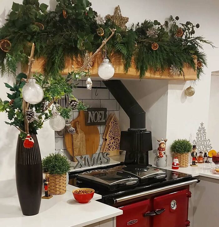 Festive kitchen decor with greenery, ornaments, and Christmas-themed signs above a red stove.