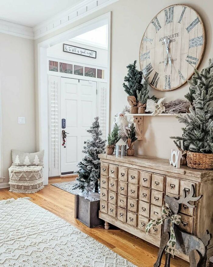 Cozy entryway with Christmas-decorating-ideas, featuring a wooden cabinet, festive trees, and a large vintage clock.