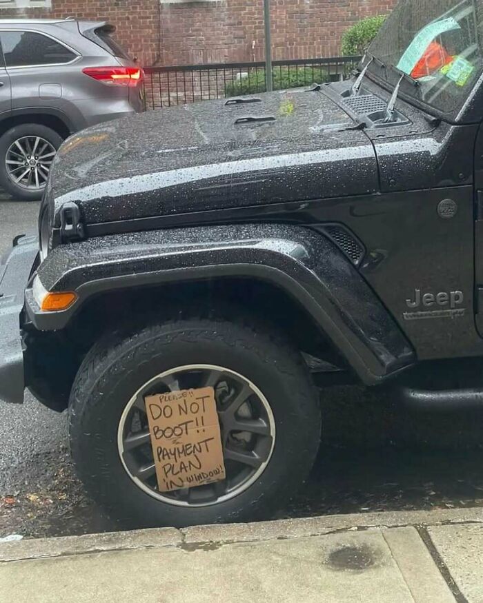 Wet Jeep parked on a New York street with a funny sign on the wheel saying, "Do not boot!! Payment plan in window!"