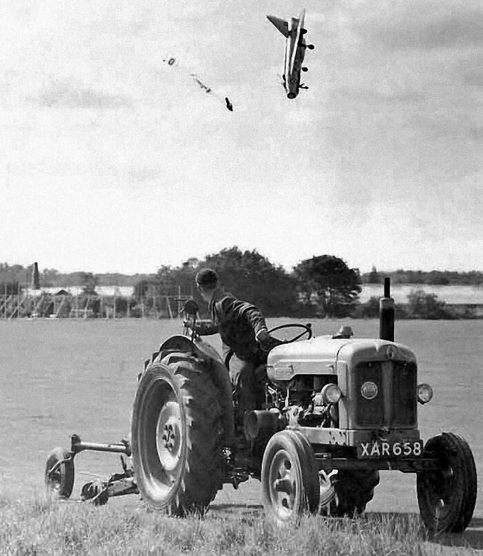 A tractor in a field with a dramatic plane crash in the background, capturing an interesting history moment.