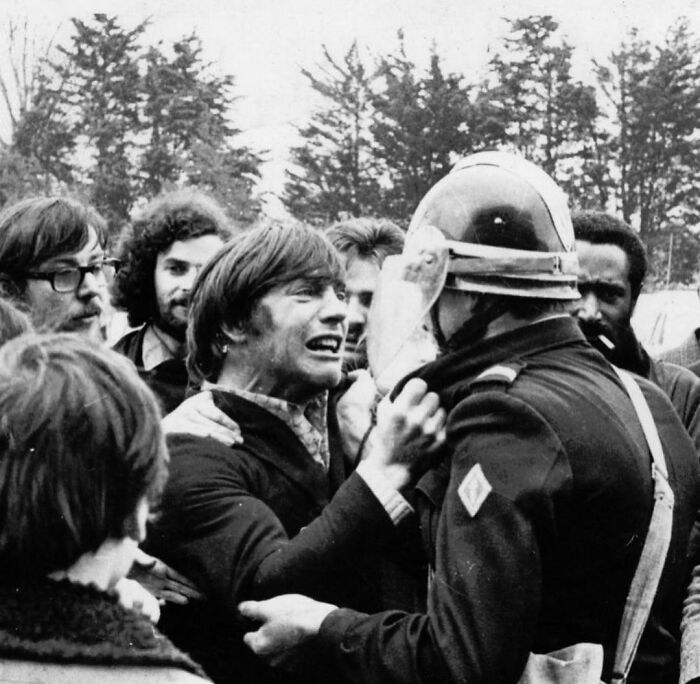 A protester confronts a police officer during a historic protest, surrounded by a group of onlookers.