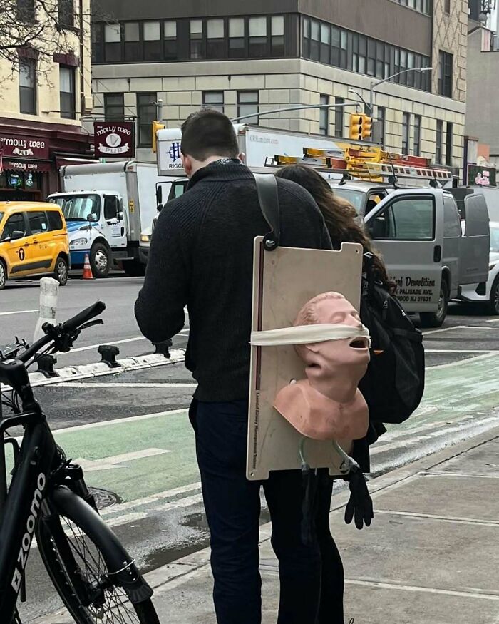 Man in New York with a mannequin head on his back, amusing street scene.