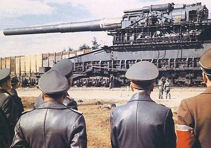 Military officers observing a historical, large-caliber railway gun, showcasing interesting history facts and technology.