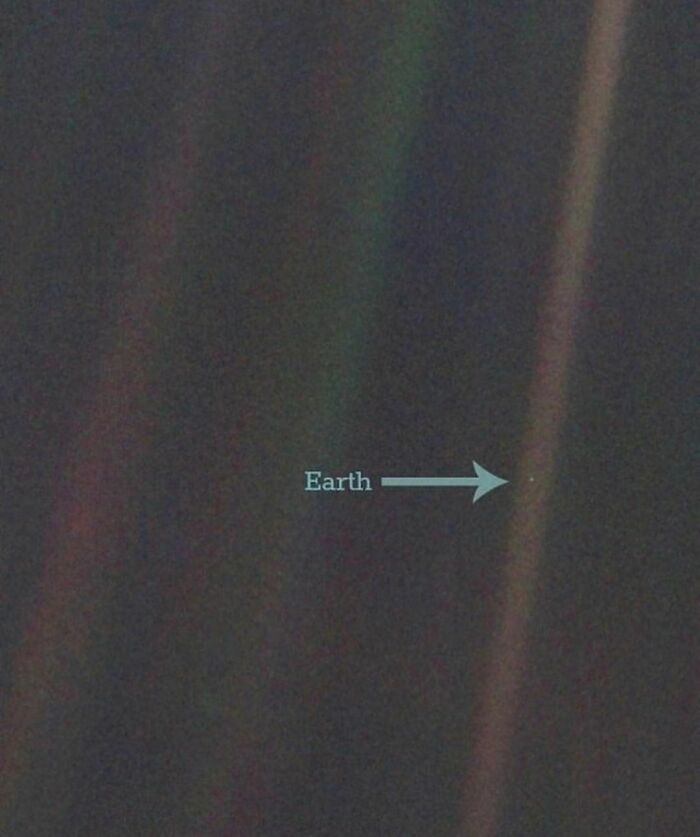 "Pale Blue Dot photo of Earth from space with an arrow pointing at the tiny dot, showcasing interesting history pics facts."