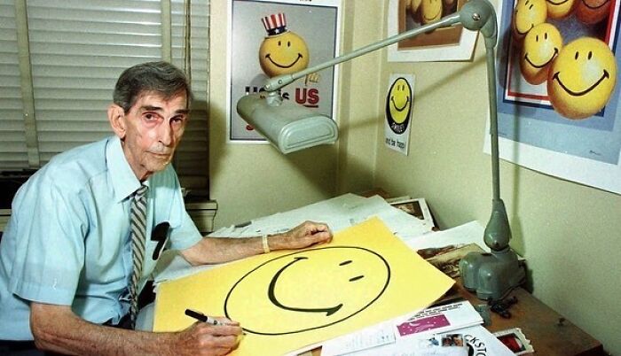 Man creating a smiley face artwork in an office full of similar posters, related to interesting history pics facts.