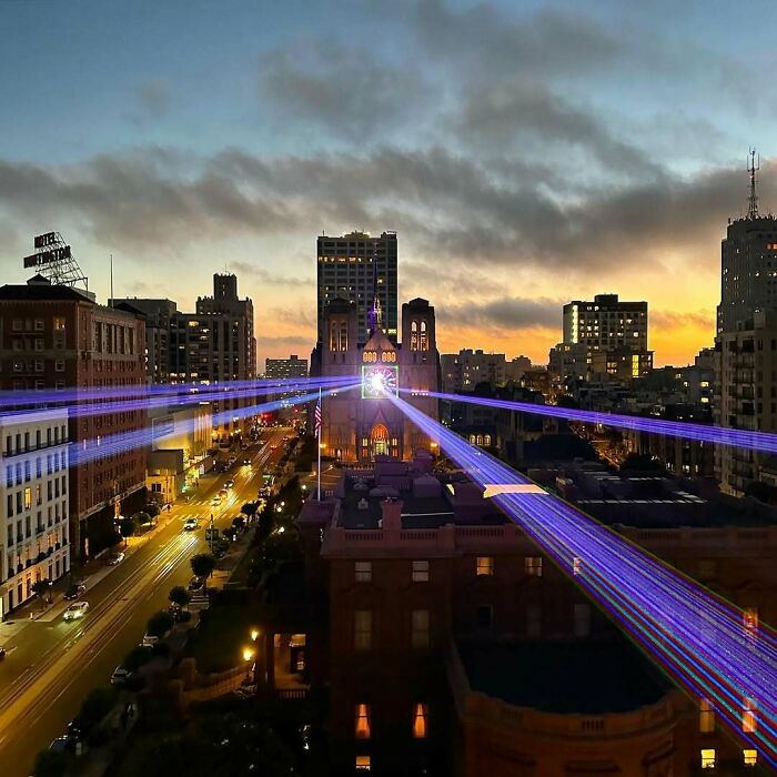 Cityscape at sunset with vibrant laser beams, resembling a videogame scene.