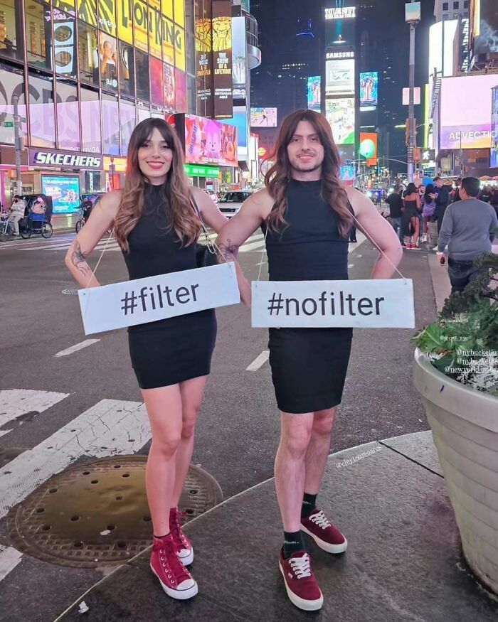 Two people in New York holding signs saying #filter and #nofilter, wearing matching outfits in Times Square.