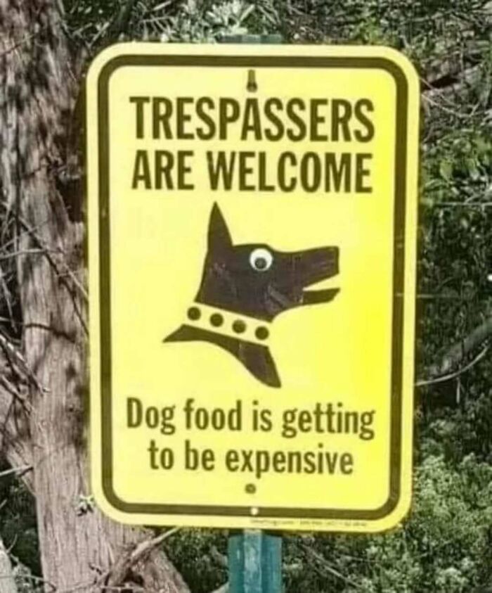 Yellow sign with dog silhouette humorously warns trespassers due to expensive dog food.