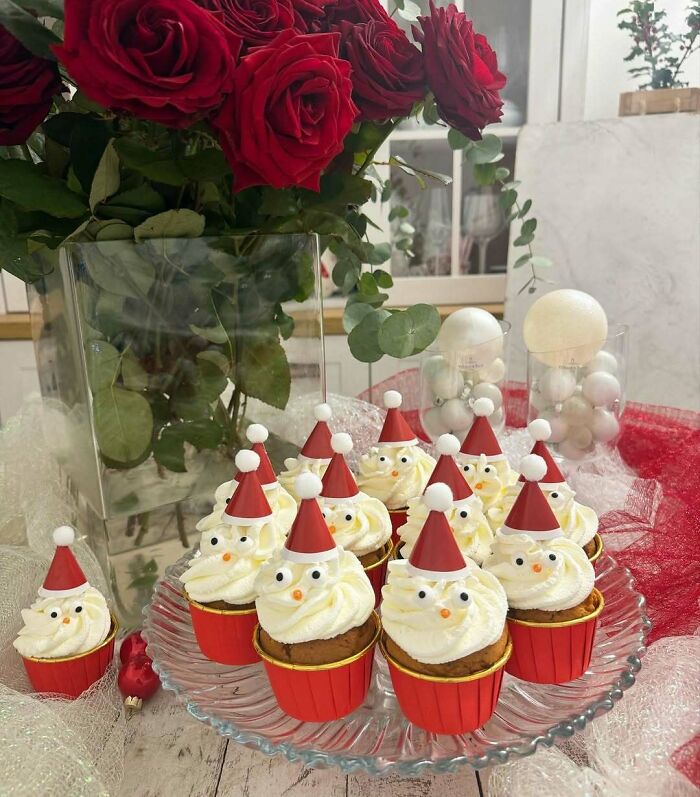 Christmas snack cupcakes with Santa hats on a glass plate next to a vase of red roses.