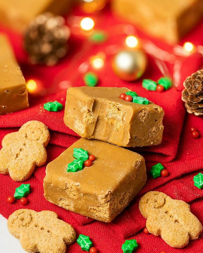 Festive Christmas snack food with fudge, gingerbread cookies, and decorative holly on a red cloth.