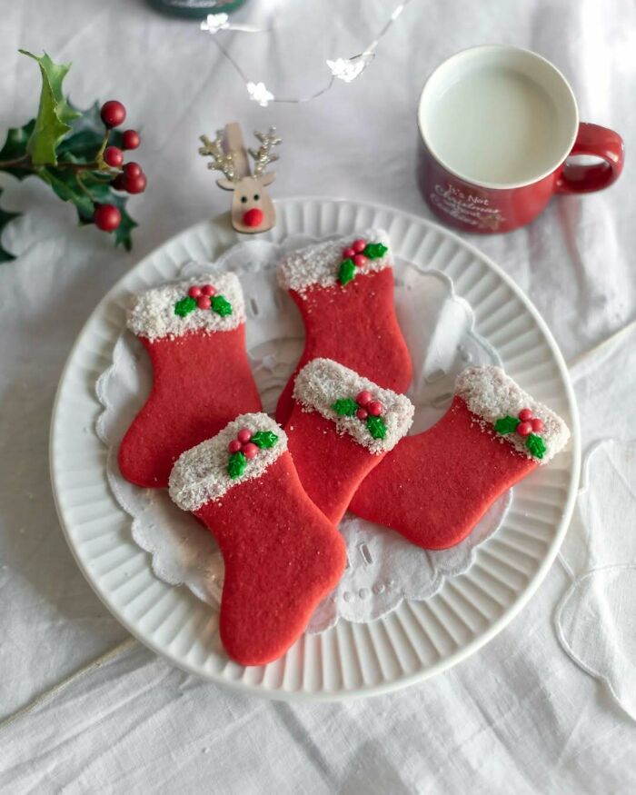 Plate of Christmas stocking cookies with festive decorations next to a cup of milk.