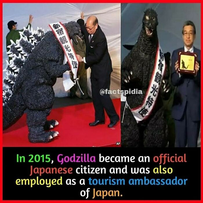 Godzilla, in costume with sash, being named a tourism ambassador of Japan in a formal setting.