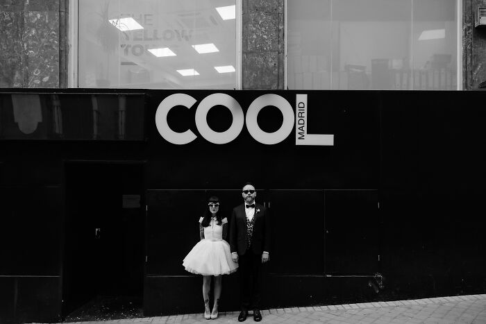 Bride and groom in stylish attire pose in front of COOL Madrid sign, showcasing top wedding photography of 2024.