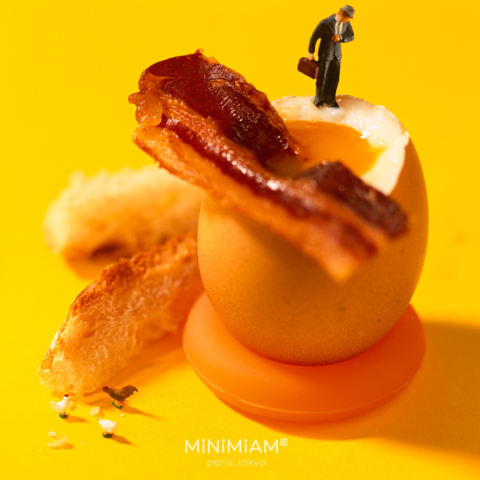 Miniature figure on soft-boiled egg with bacon, showcasing creative tiny world of foods.