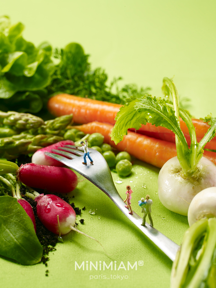 Tiny figures on a fork among fresh vegetables, showcasing creative miniatures.