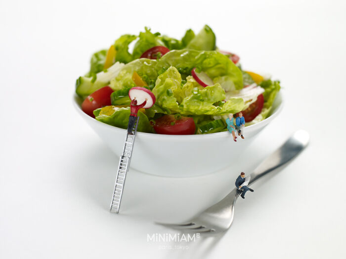 Miniature figures interacting with a salad, showcasing creative tiny world of foods in a bowl.