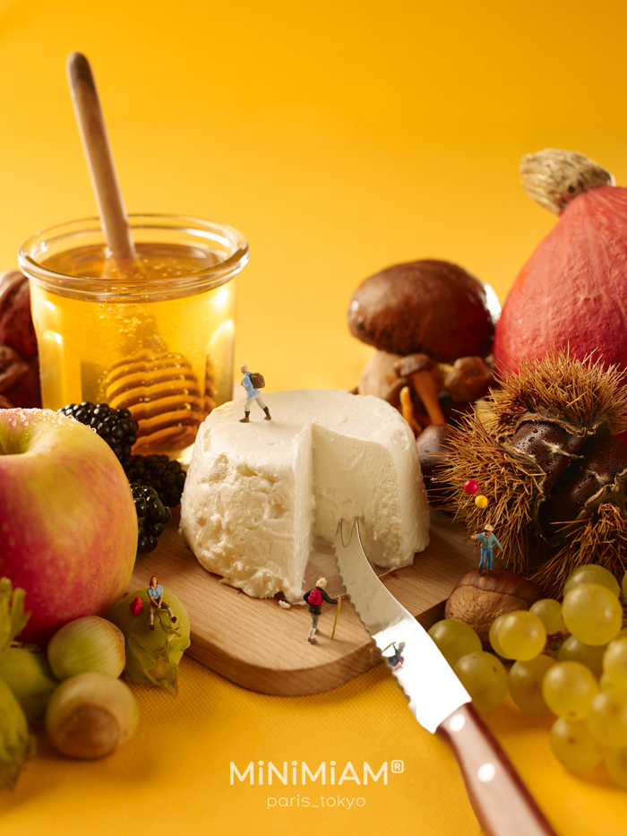 Miniatures exploring a cheese platter with honey, fruit, and nuts, showcasing creative tiny world of foods and things.