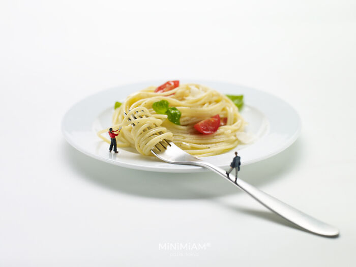 Miniature figures interacting with a plate of spaghetti, showcasing creative tiny world foods.