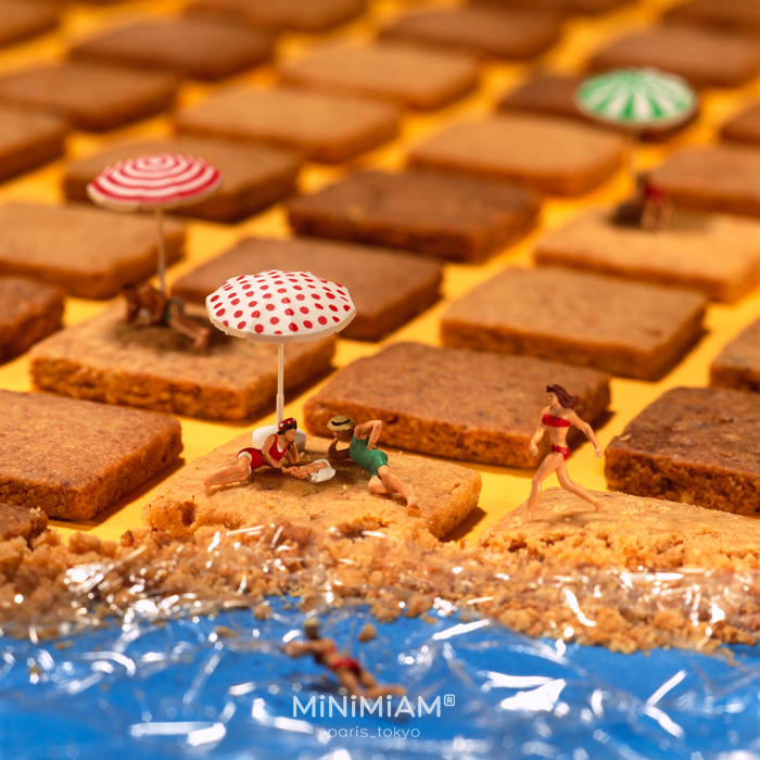 Miniatures of people on a cookie beach with umbrellas, showcasing the tiny world of foods and things.