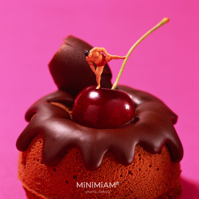 Miniature figure on a chocolate-covered cake with cherry, showcasing creative tiny world of foods.