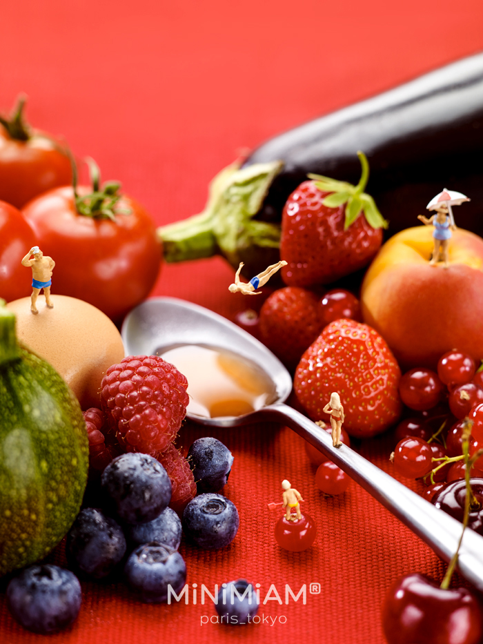 Miniatures of people amid fresh fruits like strawberries and blueberries, showcasing a tiny world of foods.