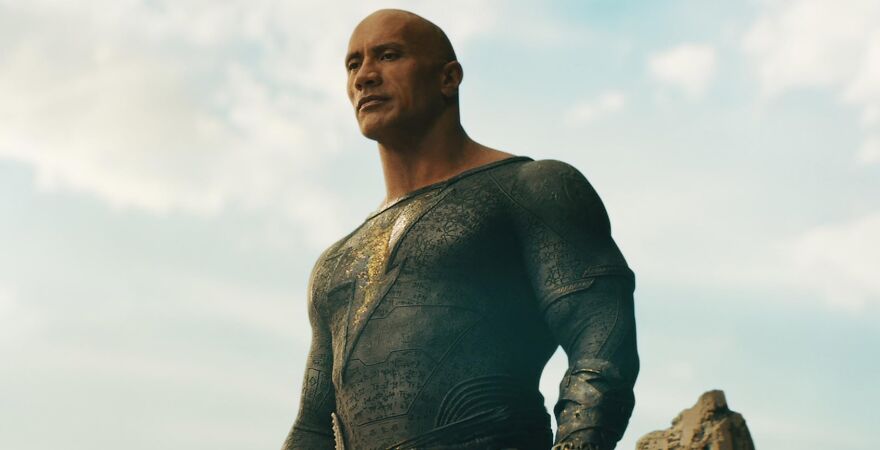 Actor Dwayne The Rock Johnson in a superhero costume standing confidently against a cloudy sky, embodying the essence of actors who always play themselves.