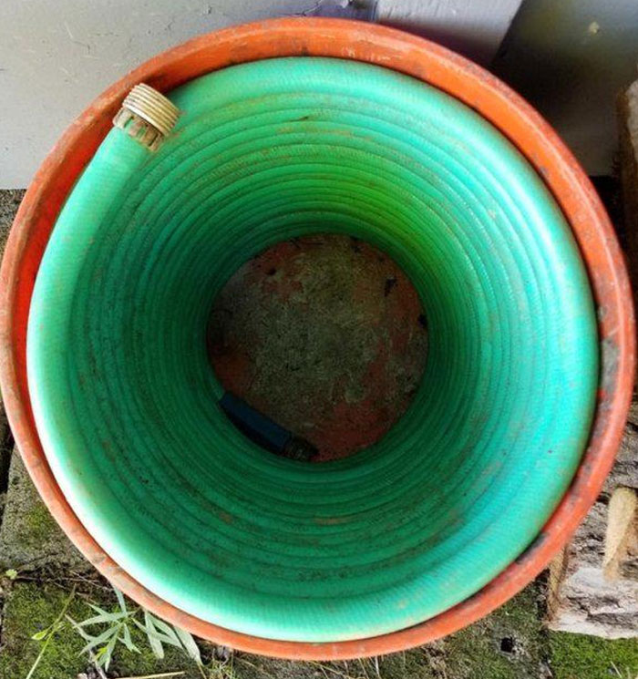 Perfectly coiled green hose fitting neatly into an orange bucket, showcasing a satisfying perfect fit.