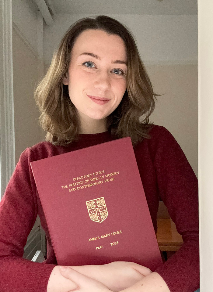 Dr. Ally Louks holding her thesis titled "Olfactory Ethics: The Politics of Smell" in a maroon cover.