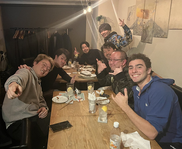 Luigi Mangione with friends, smiling and giving thumbs-up, enjoying dinner in a cozy restaurant setting.