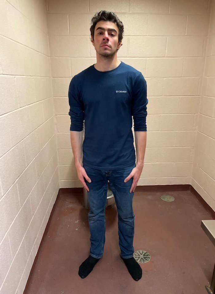 Luigi Mangione in a blue shirt standing in a room.