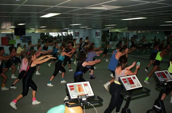 Group workout in an 80s gym, with people in vibrant fitness attire.