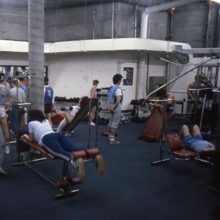 People exercising in an 80s gym with vintage fitness equipment and attire.