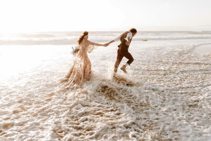 Bride and groom joyfully running through ocean waves, showcasing one of the top wedding photos of 2024.