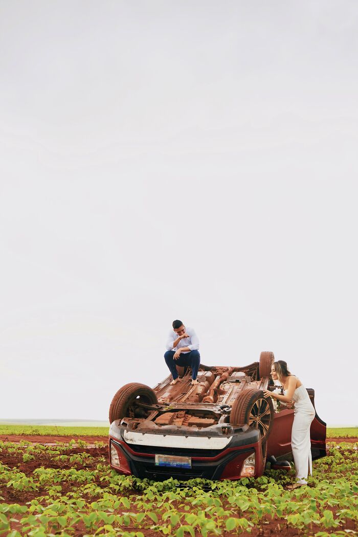 Couple poses by overturned car after accident, capturing unique photo shoot moment on the roadside field.