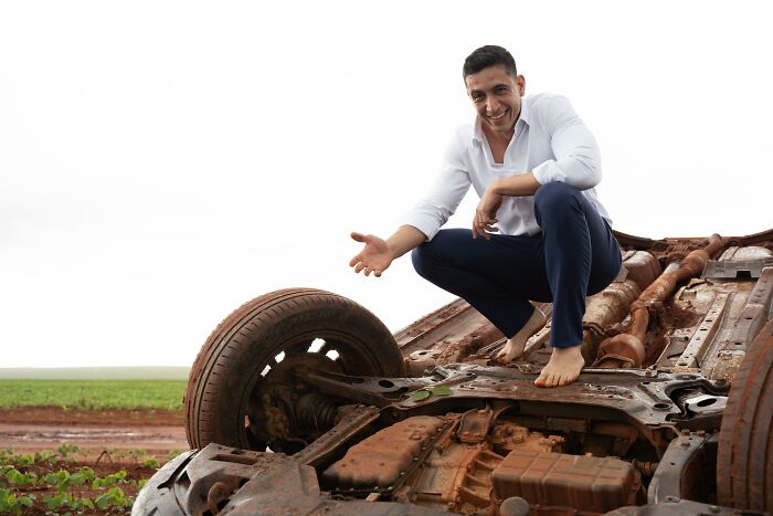 Man posing with overturned car at accident scene.