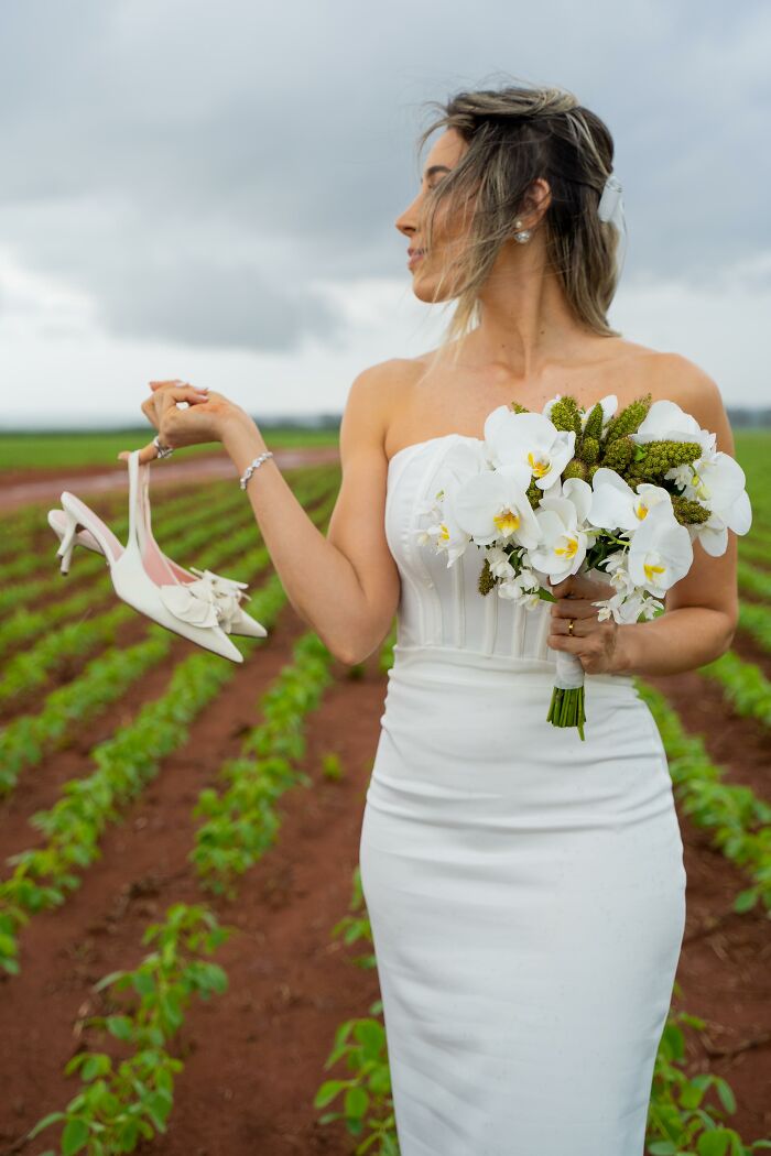 Bride holding shoes and bouquet in a field after a car accident on the way to a photoshoot.