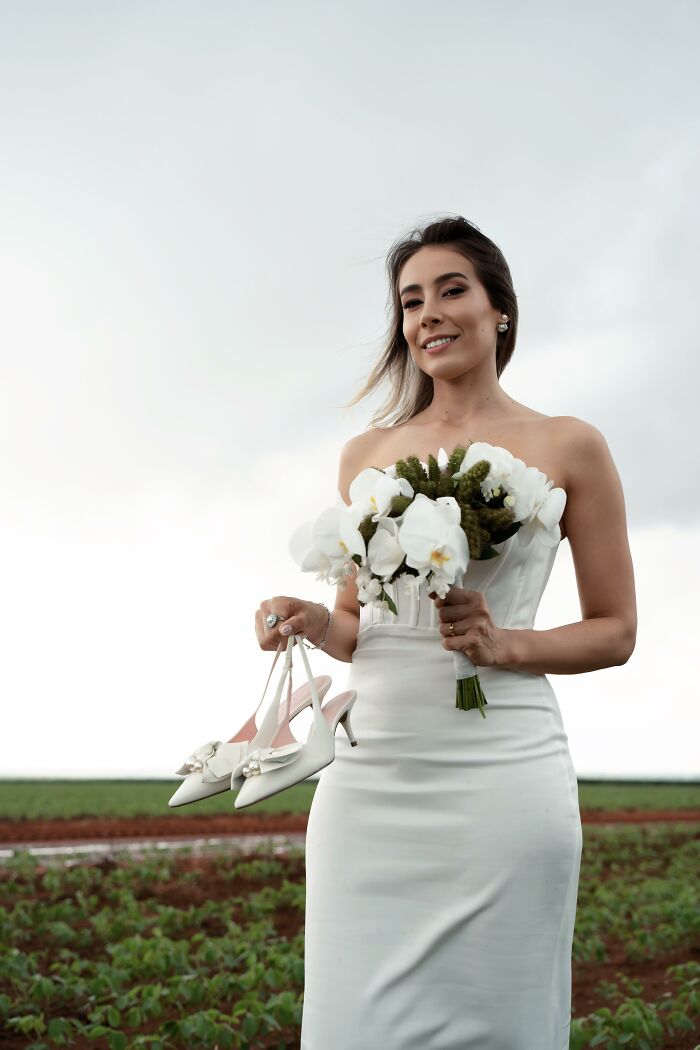 Bride holding shoes and flowers, smiling after a car accident, photo shoot at the accident scene.