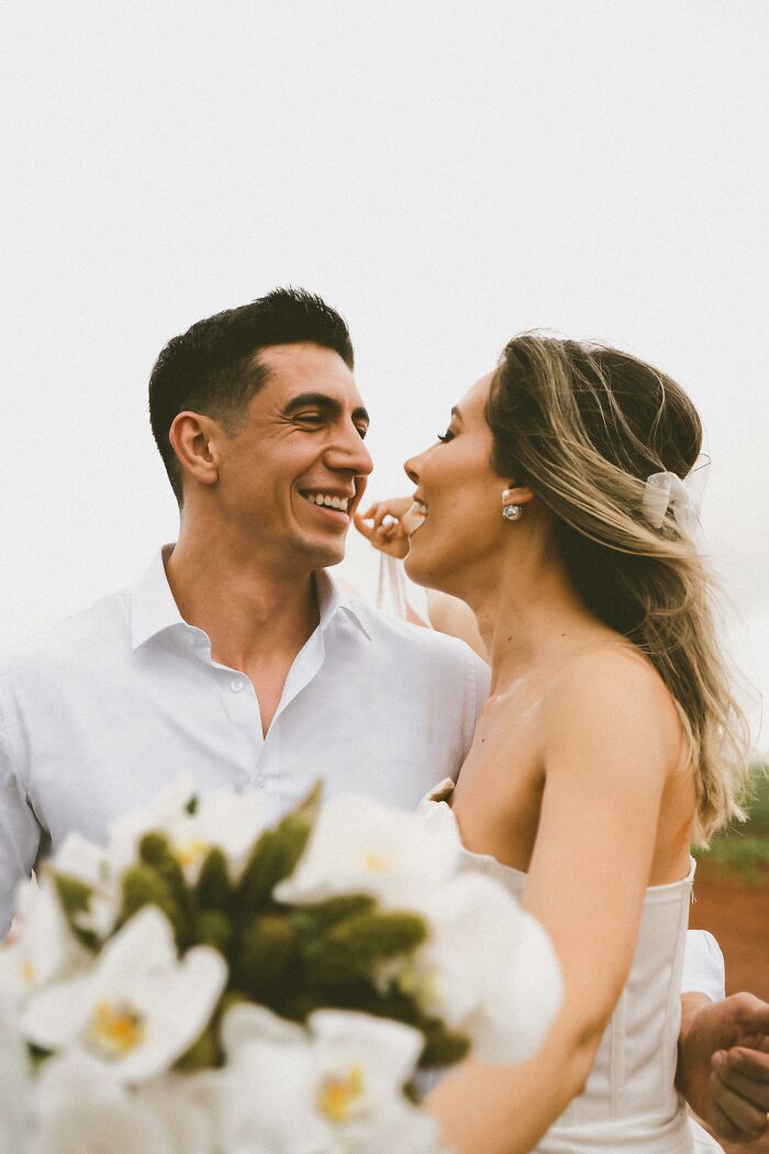 Smiling couple in wedding attire, holding flowers, capturing a unique photo moment.