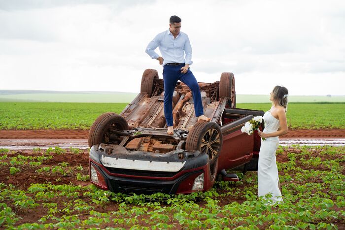 Couple takes photos beside overturned car in a field after accident on way to photo shoot.