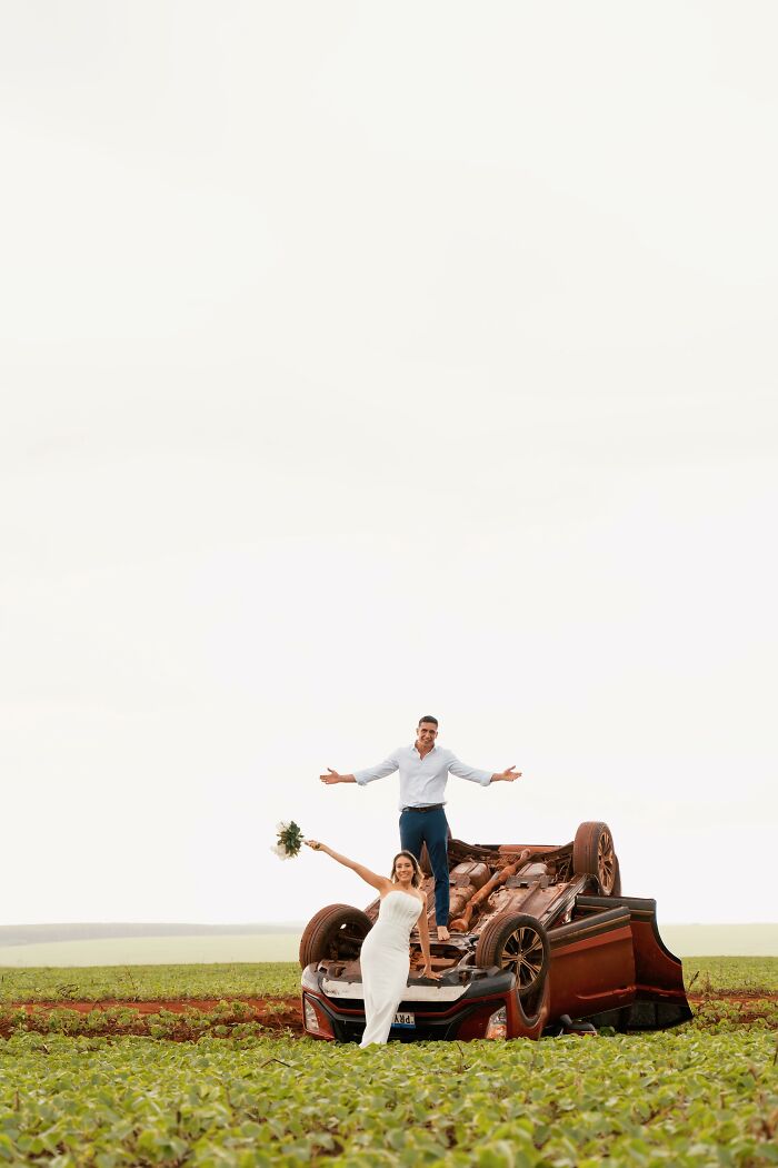 Couple poses smiling on overturned car after accident on the way to a photo shoot.