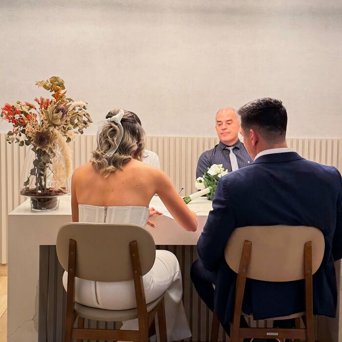 Couple at a table with a bouquet, dressed in wedding attire, captured during their unique photo shoot.