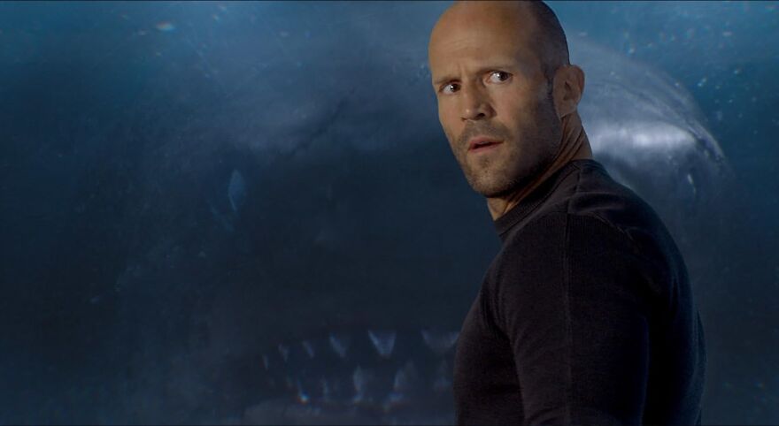 Bald actor Jason Statham in a tense scene with a giant shark in the background, exemplifying actors who always play themselves.