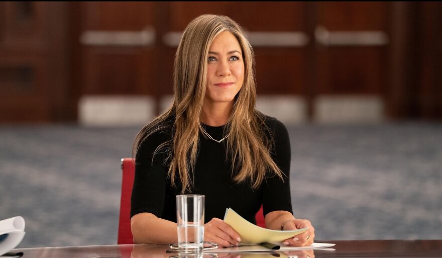 Actress Jennifer Aniston at a table with papers and a glass, characteristic role style, exemplifying actors who always play themselves.