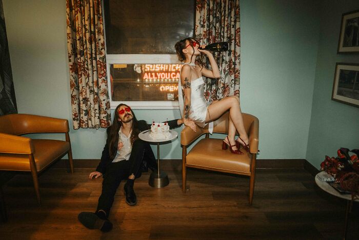 A couple in a playful wedding scene, the bride on a chair drinking from a bottle, showcasing top wedding photos of 2024.