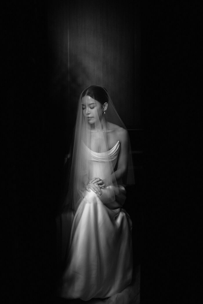 Elegant bride in veil, captured in a top 2024 wedding photo, sitting gracefully in a dimly lit setting.