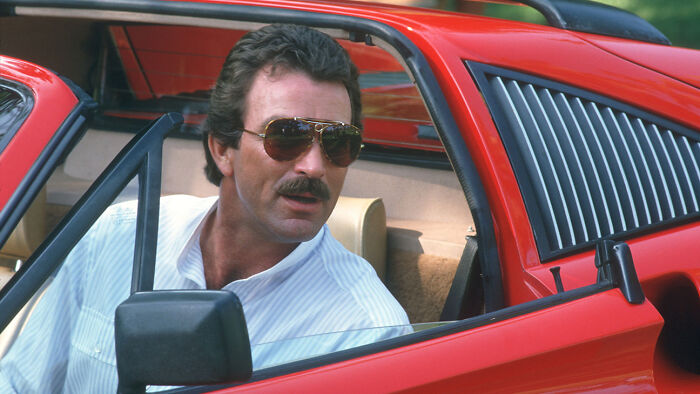 Man with sunglasses in a white shirt sits in a red car, relating to fascinating fan theories.