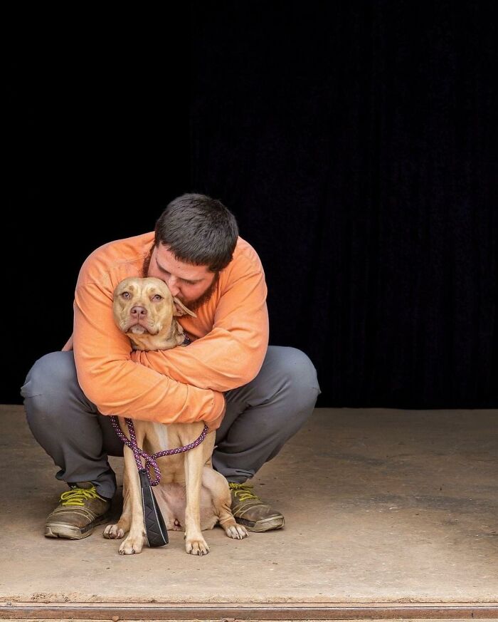 Man in an orange shirt hugging a rescued dog with a purple leash.