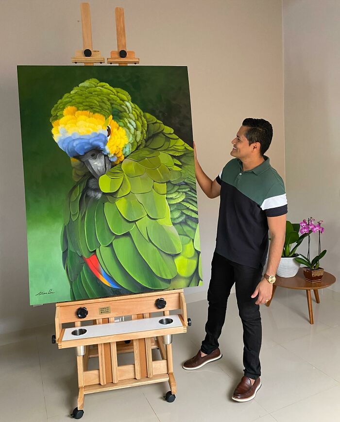 Brazilian artist with a vibrant parrot painting on an easel.